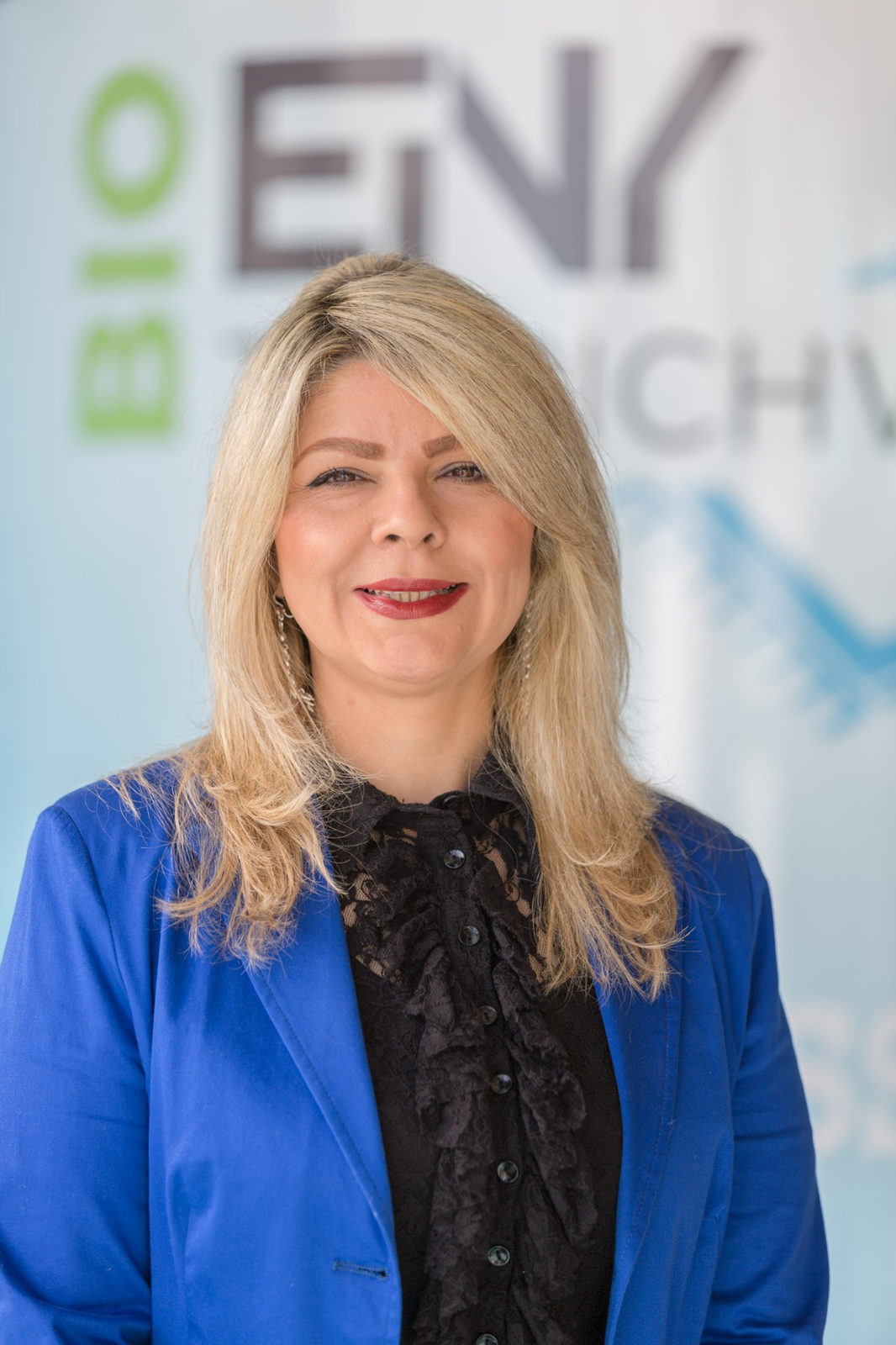 Portrait von Mitra Einy, verantwortlich für Organisation und Kundenbetreuung bei Bio Teppichwäsche Einy in Salzburg, vor dem Firmenlogo.