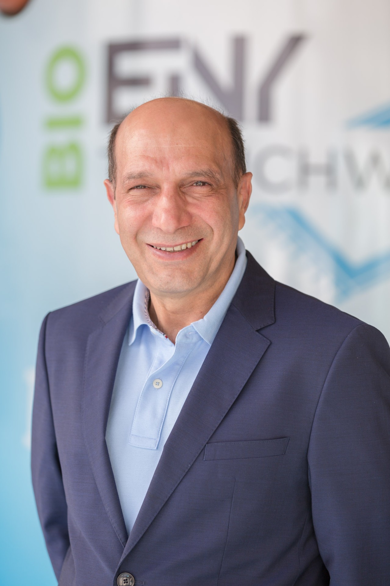 Portrait von Bahram Einy, Seniorchef in Pension der Bio Teppichwäsche Einy in Salzburg, vor dem Firmenlogo.